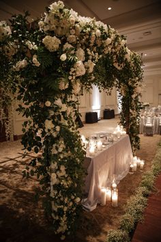 a table with candles and flowers on it in front of an arch decorated with greenery