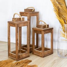 three wooden lanterns sitting on top of a floor next to a vase and palm tree