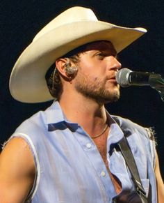 a man wearing a cowboy hat and holding a guitar in his right hand while singing into a microphone