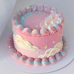 there is a pink and blue cake with clouds on the top that has rainbow icing