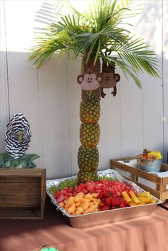 a table topped with a tray of fruit and a monkey decoration on top of it