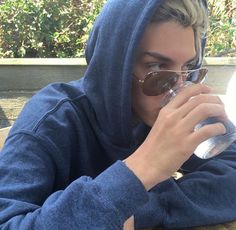 a man in a blue hoodie drinking out of a glass with sunglasses on his head