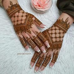 two hands with henna designs on them and a flower in the background, one is pink