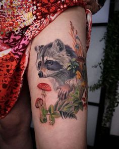 a raccoon tattoo on the thigh with flowers and leaves around it's legs