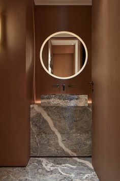 a bathroom with marble counter tops and brown walls, along with a round mirror on the wall