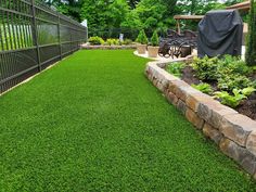 an artificial lawn in a backyard with stone retaining wall and fence surrounding the yard area