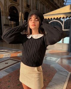 a woman in a black sweater and skirt posing for the camera with her hands on her head