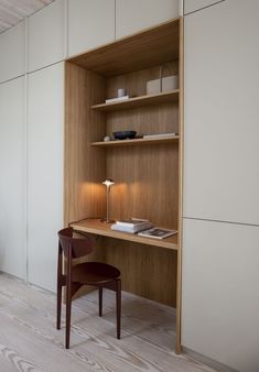 a wooden desk and chair in a room with white walls, wood flooring and open shelving