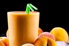 an orange smoothie with a green straw in front of peaches