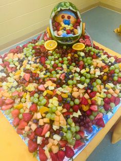 a table topped with lots of fruit on top of a plastic tray filled with watermelon, oranges and grapes