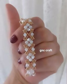 a woman's hand holding a gold and white beaded bracelet