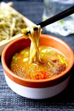 a bowl of soup with chopsticks sticking out of it and noodles in the background