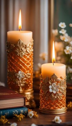 two lit candles sitting on top of a wooden table next to flowers and an open book