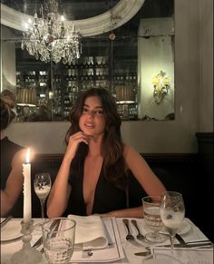 a woman sitting at a table with a candle in front of her and wine glasses on the table