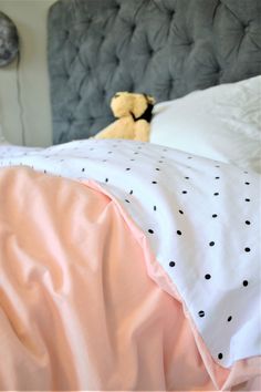 a teddy bear sitting on top of a bed next to a pink comforter and pillows