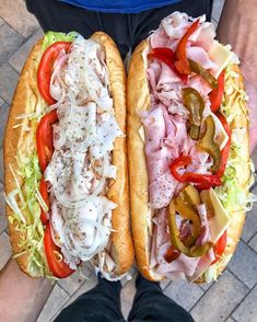 two sub sandwiches with meat, cheese and vegetables on them are being held by someone's hands