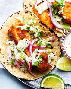 two fish tacos with cole slaw, cilantro and lime wedges