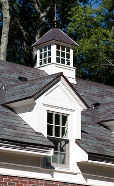 a clock tower on top of a white building with black shingles and brick walls