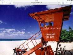 an orange lifeguard stand on the beach with a bike parked under it and people walking around