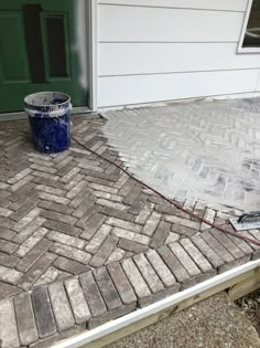 a bucket sitting on the ground next to a green door and a brick walkway in front of a house