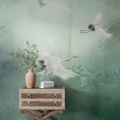 two white birds flying in the sky above a table with a vase and book on it