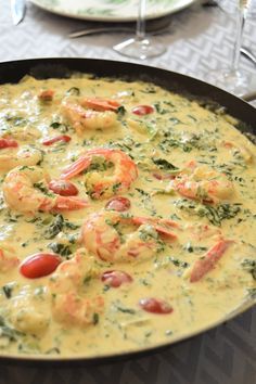 a pan filled with shrimp and cheese on top of a table next to wine glasses