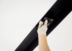 a person in white gloves is holding up a black ceiling beam with one hand and the other