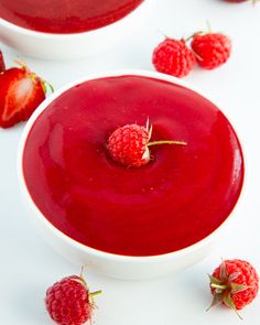 two white bowls filled with raspberry sauce and fresh strawberries scattered around them