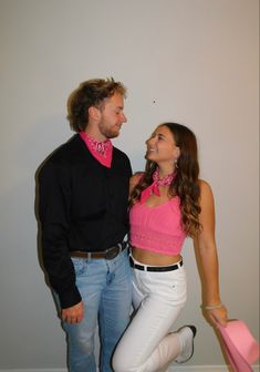 a man standing next to a woman in white pants and a pink shirt with black collar