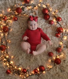 a baby is sitting on the floor surrounded by christmas decorations and lights, smiling at the camera