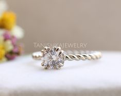 a white diamond ring sitting on top of a table next to some yellow and purple flowers