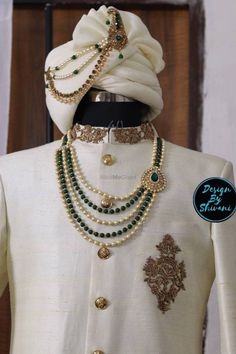 a man wearing a white turban with green and gold beads on his neck