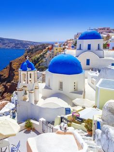 some white and blue buildings on the side of a hill with water in the background