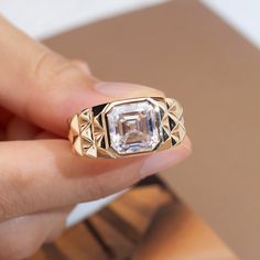 a woman's hand holding a ring with an emerald stone in the center and gold filigrees around it