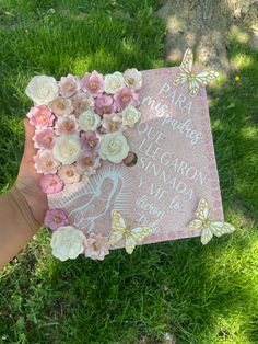 a person holding up a pink and white card with flowers on it in the grass