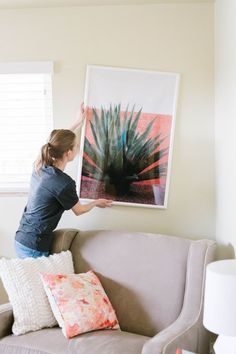 a woman is holding up a painting on the wall above a couch in her living room