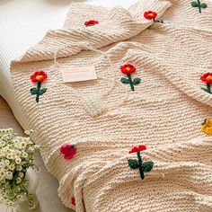 a crocheted blanket with red and yellow flowers on it sitting on a bed