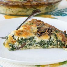 a slice of quiche with spinach and mushrooms on a white plate next to a pie dish