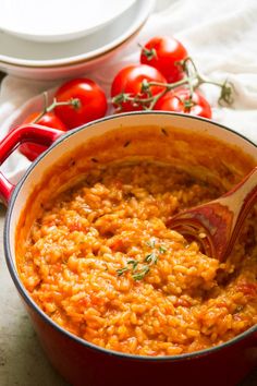 a red pot filled with food next to tomatoes