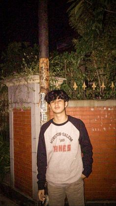 a young man standing next to a brick wall