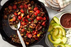 a skillet filled with vegetables and rice next to a bowl of sauce on the side