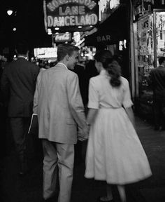 a man and woman walking down a street holding hands in front of a neon sign