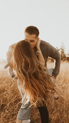 a man and woman kissing in the middle of a field with long hair blowing in the wind