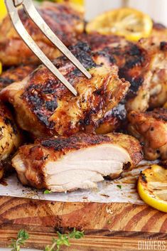 someone is cutting up some chicken on a cutting board with lemons and parsley