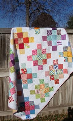 a quilt hanging from a clothes line in front of a fence