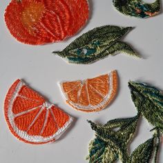 oranges and leaves are embroidered onto the back of small appliques on a white surface