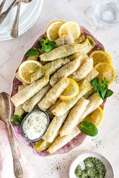 fish fillets with lemons and herbs on a platter next to silverware