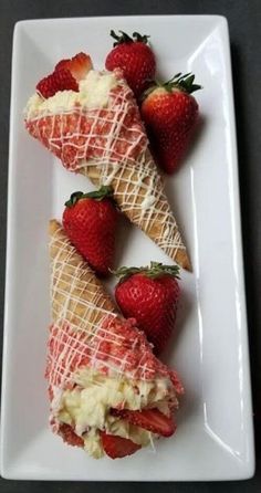 some strawberries are on a white plate and one is cut in half to look like ice cream