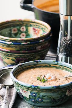 there is a bowl of soup next to two bowls with spoons on the table