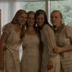 four women in white dresses standing next to each other with their arms around one another